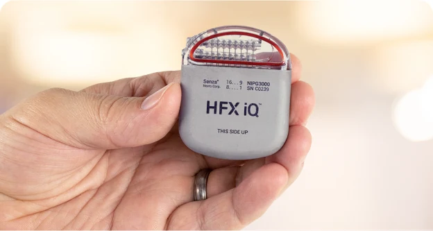 A hand holding the Nevro HFX iQ generator, a small grey implant with a clear connector block on top